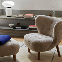 Cozy beige upholstered chair with a soft, textured surface and light wood legs, paired with a deep blue throw.