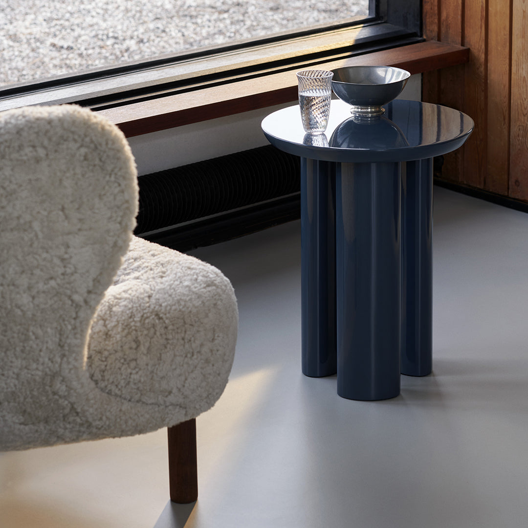 Modern navy blue accent table with cylindrical legs, complemented by a textured cream chair and minimalist decor.