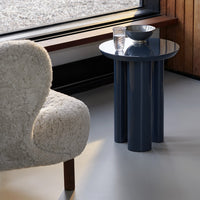 Modern navy blue accent table with cylindrical legs, complemented by a textured cream chair and minimalist decor.