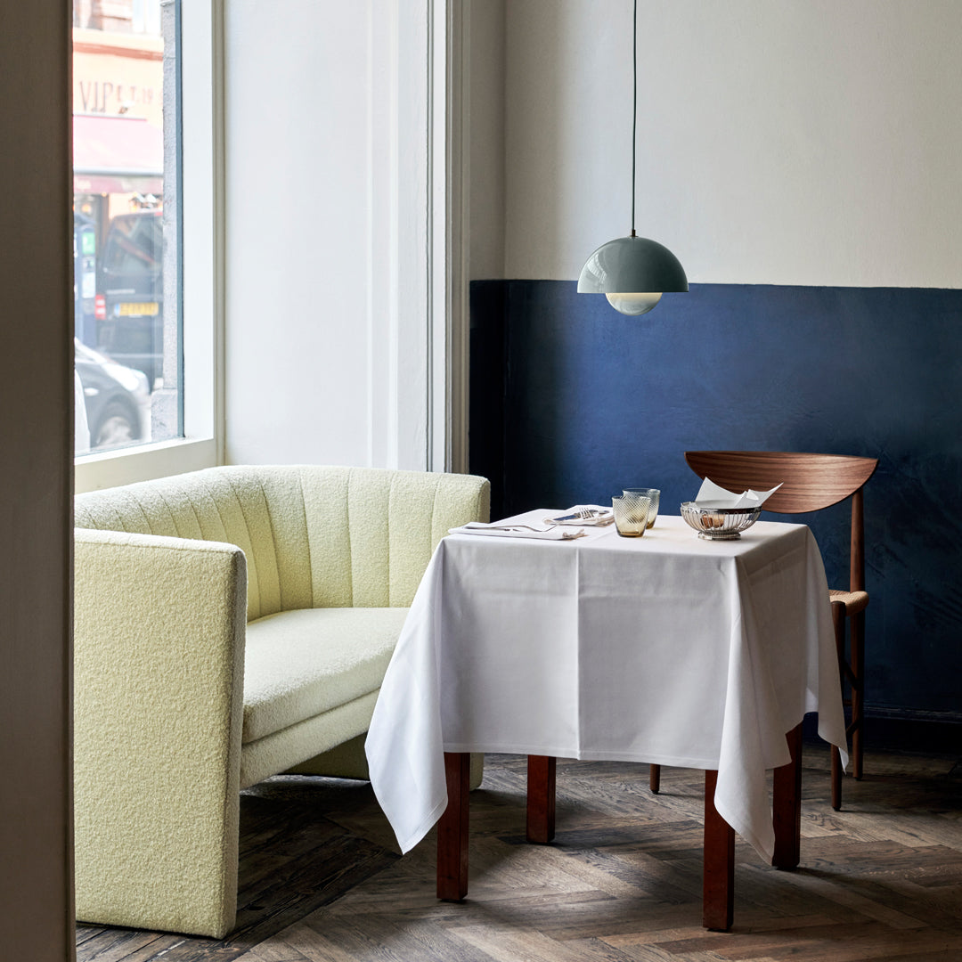 Soft yellow-green sofa, sleek dark blue wall, and crisp white tablecloth create a modern, inviting dining atmosphere.