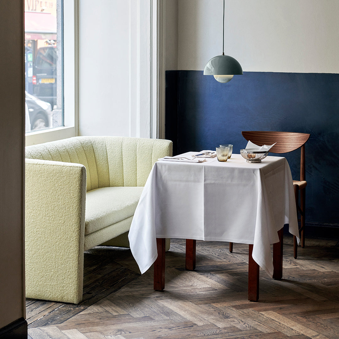 Soft pastel yellow sofa, crisp white tablecloth, rich navy blue wall, and warm wood floor create a modern dining aesthetic.