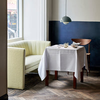 Soft pastel yellow sofa, crisp white tablecloth, rich navy blue wall, and warm wood floor create a modern dining aesthetic.
