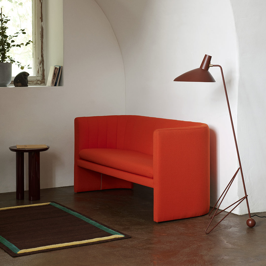 Bold orange sofa with minimalist design, complemented by a geometric rug with green and beige accents.