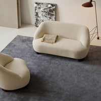 Cream-colored sofa with a textured fabric, set on a grey plush rug, featuring a minimalist design.