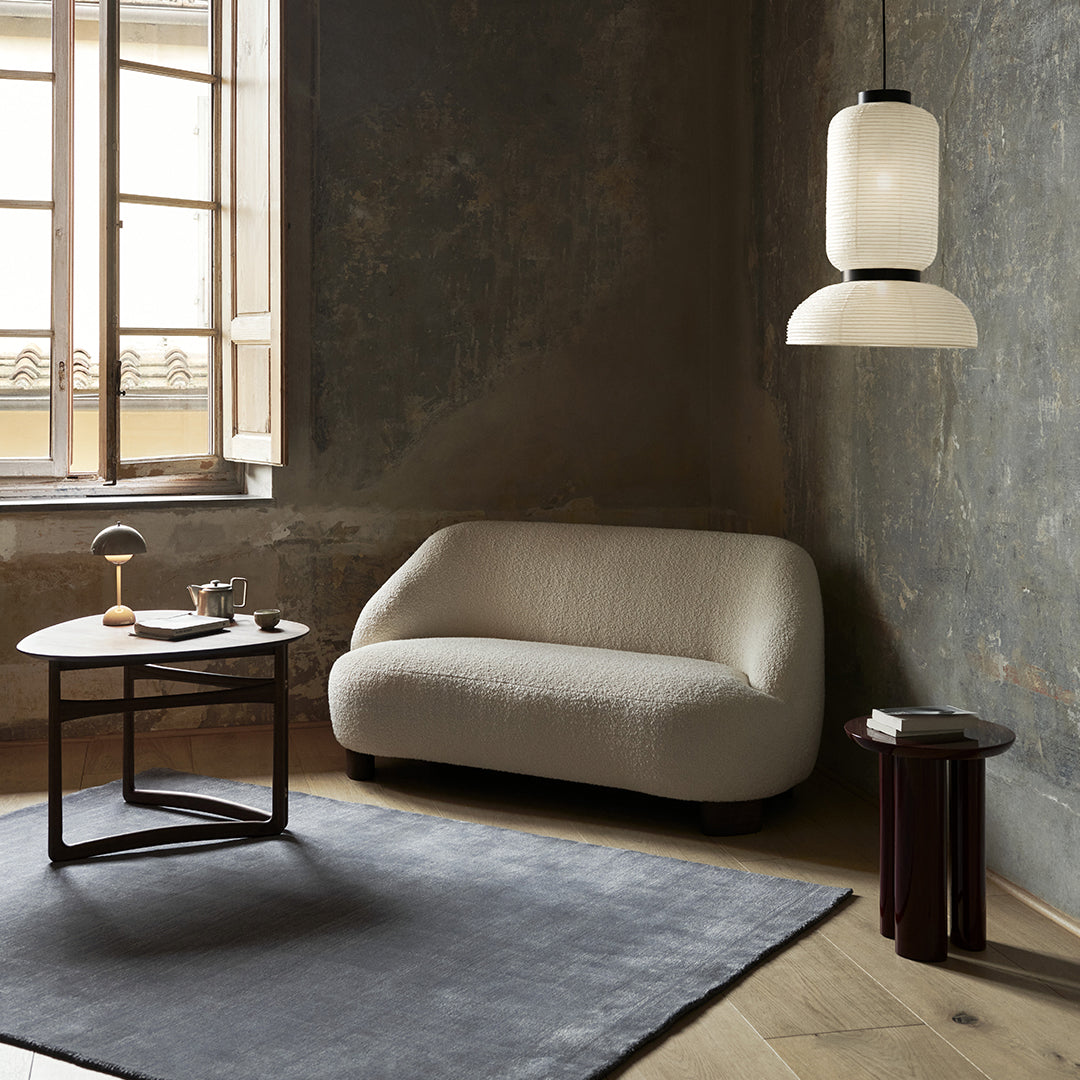 Light beige curved sofa, dark wood side tables, charcoal gray rug, and soft white pendant light in a rustic setting.