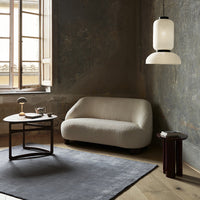 Light beige curved sofa, dark wood side tables, charcoal gray rug, and soft white pendant light in a rustic setting.