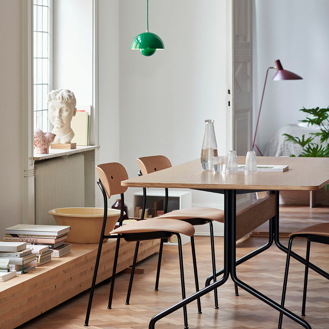 Minimalist dining table with light wood finish, paired with black metal legs, accented by green and pink decor.