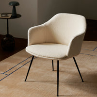 Cream upholstered chair with a textured finish and sleek black metal legs, set against a neutral-toned rug.