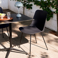 Black modern chair with a smooth surface, set against a stylish outdoor table and green foliage backdrop.
