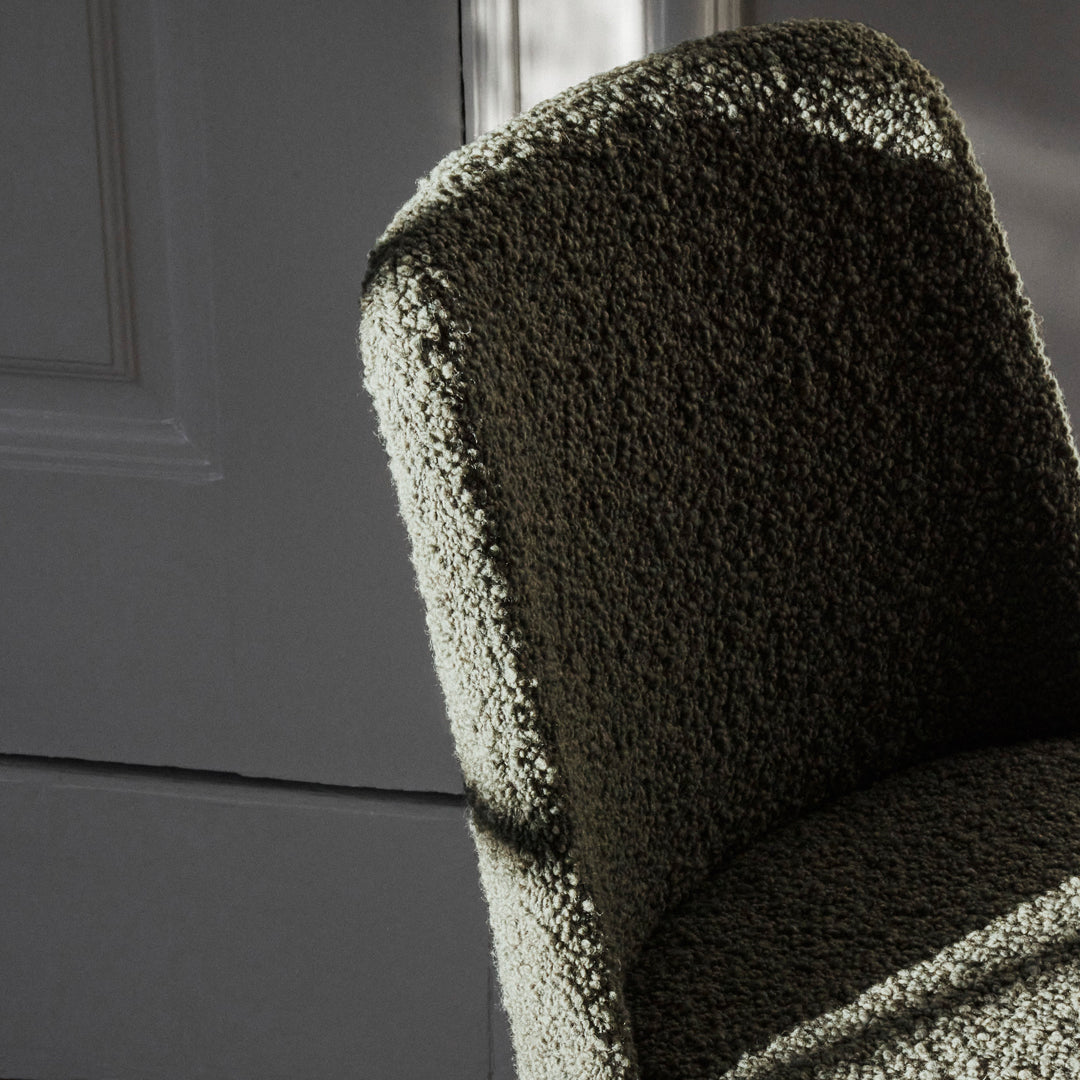 Olive green textured chair with a soft, plush surface and rounded back, casting gentle shadows.