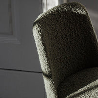 Olive green textured chair with a soft, plush surface and rounded back, casting gentle shadows.