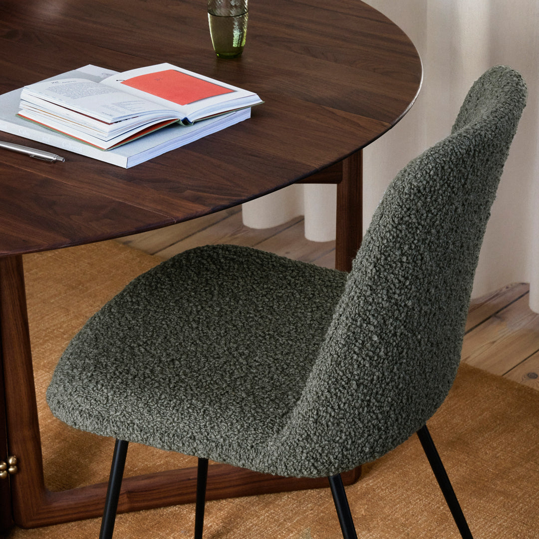 "Cozy olive green chair with textured upholstery against a warm wooden table backdrop."
