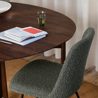 Textured green chair beside a round wooden table, with books and a glass in soft, neutral tones.