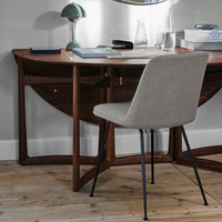 "Natural wood desk with curved edges and gray upholstered chair on light wood floor, accented by a green lamp."