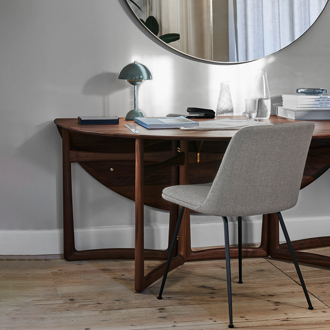 "Modern gray chair beside a sleek walnut desk, featuring a round mirror against a soft gray wall."