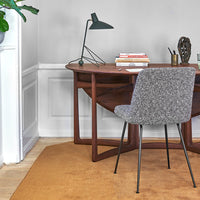 Gray patterned chair beside a wooden desk on an orange rug, with a minimalist black lamp and stylish decor.