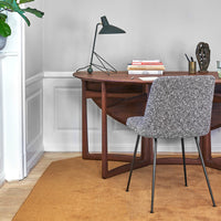 Gray patterned chair beside a wooden desk on a warm ochre rug, set against a light gray wall.