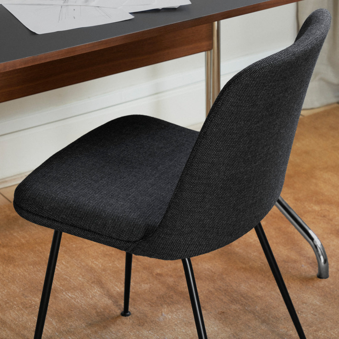Black upholstered chair with a smooth texture and sleek metal legs, set against a warm, neutral backdrop.