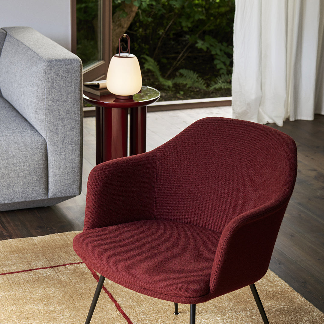 "Deep burgundy upholstered chair with smooth curves, paired with a modern gray sofa and light wood accents."