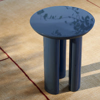 Navy blue round table with sleek, glossy finish and four cylindrical legs, on a textured beige rug.