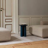 Neutral beige furniture with a deep blue side table, set on a light wood floor and accented by a patterned rug.