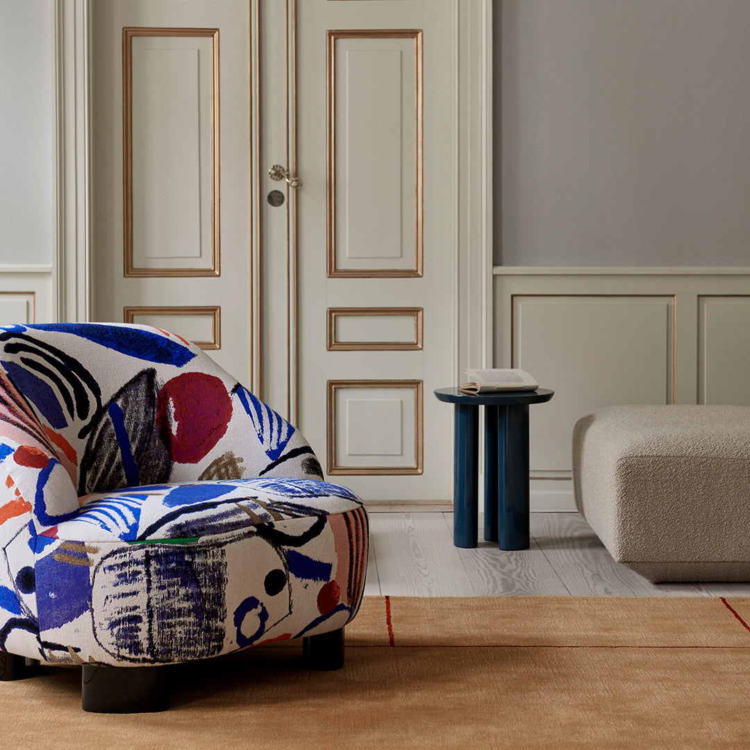 Colorful patterned armchair featuring blues, reds, and abstract designs, set against a neutral-toned room.