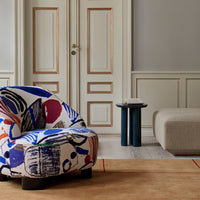 Colorful patterned armchair featuring blues, reds, and abstract designs, set against a neutral-toned room.