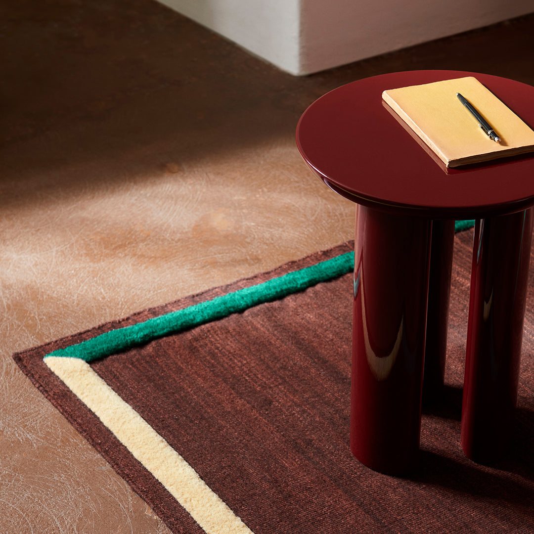 Multicolored geometric rug with brown, green, and yellow stripes, paired with a glossy burgundy side table.