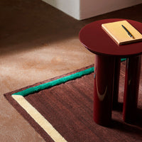 Multicolored geometric rug with brown, green, and yellow stripes, paired with a glossy burgundy side table.