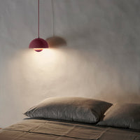 Modern pink pendant light illuminating gray bedding in a minimalist bedroom setting, creating a cozy atmosphere.