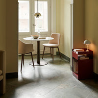 Elegant pastel chairs, light-colored round table, red storage unit, and soft gray stone floor in a cozy space.