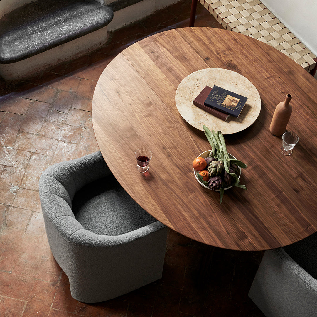 Round wooden dining table with a rich brown finish, complemented by gray upholstered chairs and a patterned table runner.