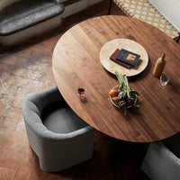 Round wooden dining table with a rich brown finish, complemented by gray upholstered chairs and a patterned table runner.