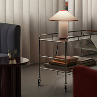 Sleek silver cart with a round white and red lamp, surrounded by muted gray, blue, and warm earth tones.