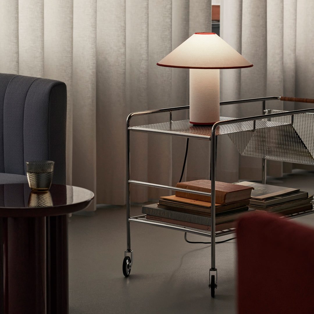 Sleek silver cart with a round white and red lamp, surrounded by muted gray, blue, and warm earth tones.