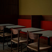 Dark wooden tables and woven chairs with red and yellow walls in a modern cafe setting. Elegant and minimalist design.