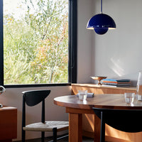 Modern dining room featuring a blue pendant light, wooden table, and black and natural woven chairs in a bright, airy space.