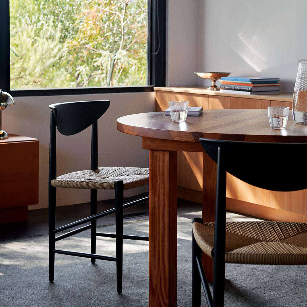 Minimalist wooden dining table with black and natural woven chairs, featuring warm wood tones and clean lines.