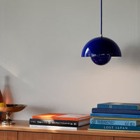 "Vibrant blue pendant lamp with a sleek semi-circular design, accenting a modern bookshelf arrangement."