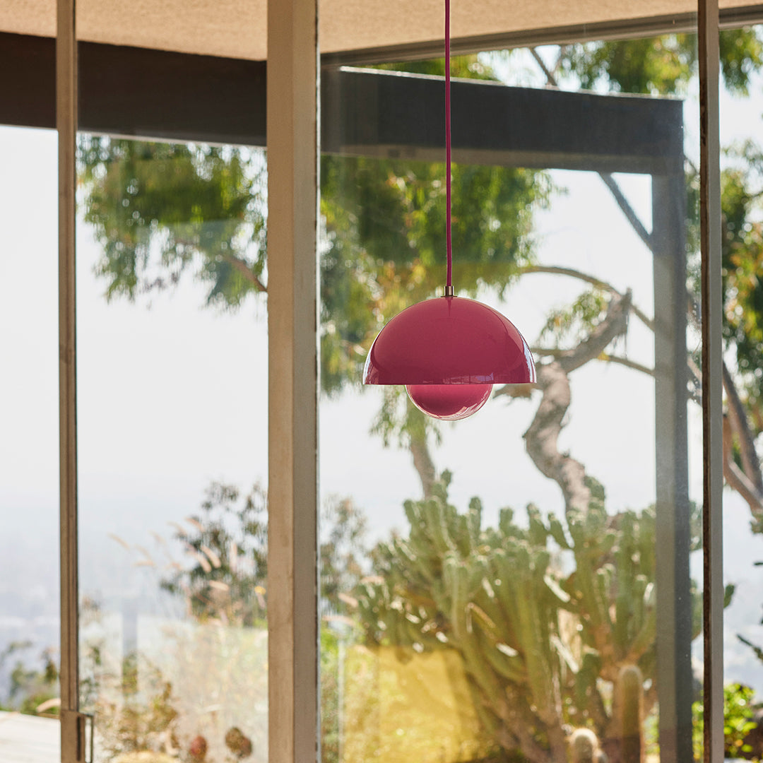 "Vibrant pink pendant light with a smooth, modern round design, set against a natural greenery backdrop."