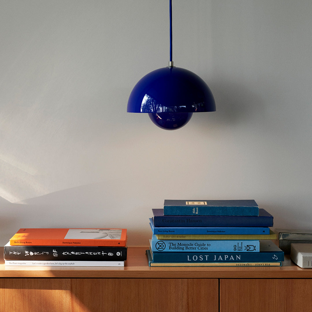 Vibrant blue pendant lamp hanging above a stack of colorful books on a wooden shelf.