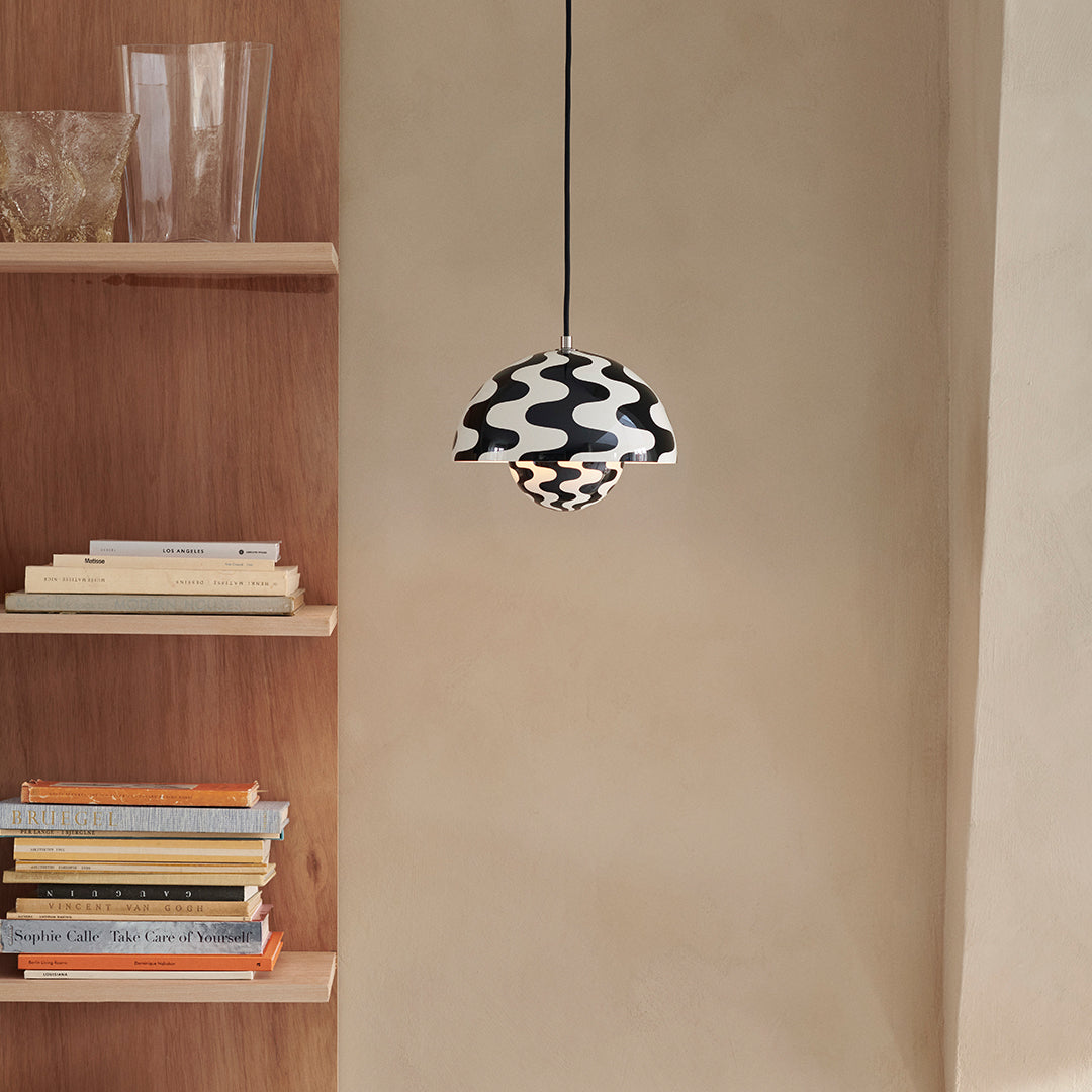 Black and white patterned pendant lamp, showcasing wavy designs, against a neutral wall and wooden shelving.
