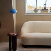 Cream textured sofa, blue pendant light, and dark wood side table with circular patterns. Soft, modern color palette.