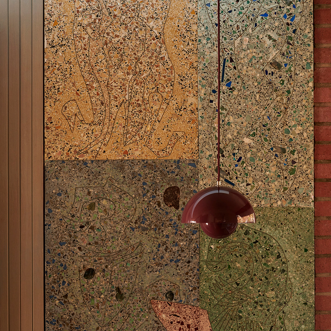 Textured wall panel in earthy tones of beige, green, and brown with colorful speckles and a modern burgundy pendant light.