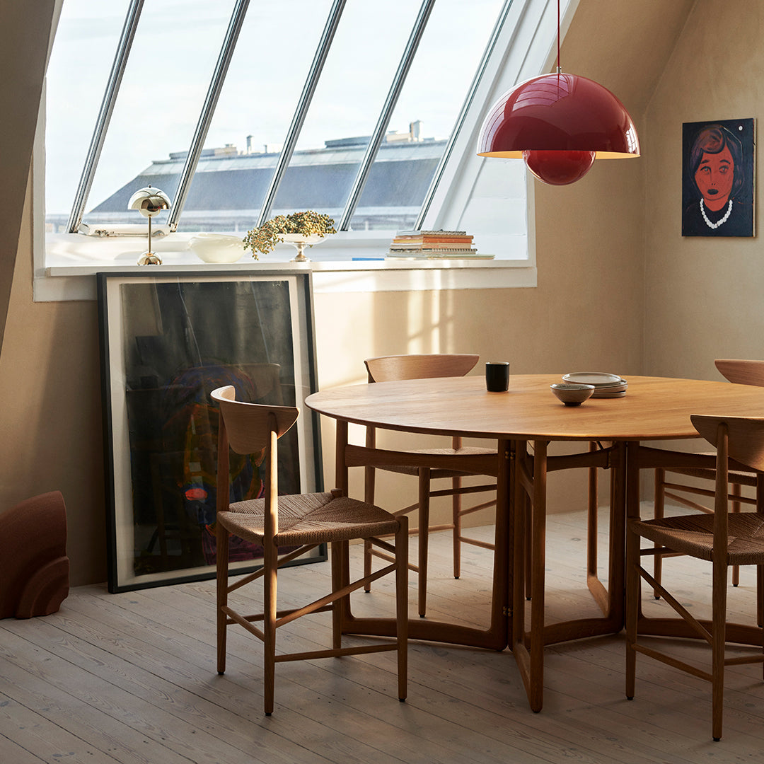 Modern wooden dining table with natural tones, complemented by red pendant light and textured wall. Bright, airy ambiance.