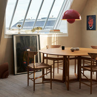 Modern wooden dining table with natural tones, complemented by red pendant light and textured wall. Bright, airy ambiance.