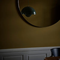 Green dome pendant light against a warm mustard wall and chic circular mirror, complemented by dark blue chair.