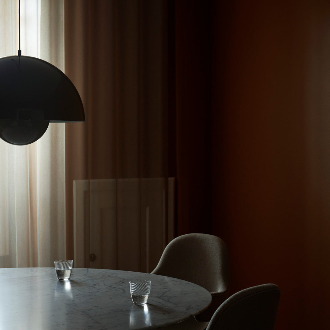 Modern dining area with warm brown walls, soft beige curtains, and a round marble table contrasted by black lighting.