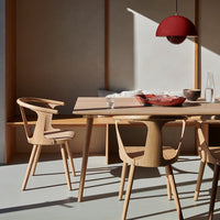 Light wood dining table with natural tones, minimalist design, and a bold red pendant light, complemented by earthy decor.