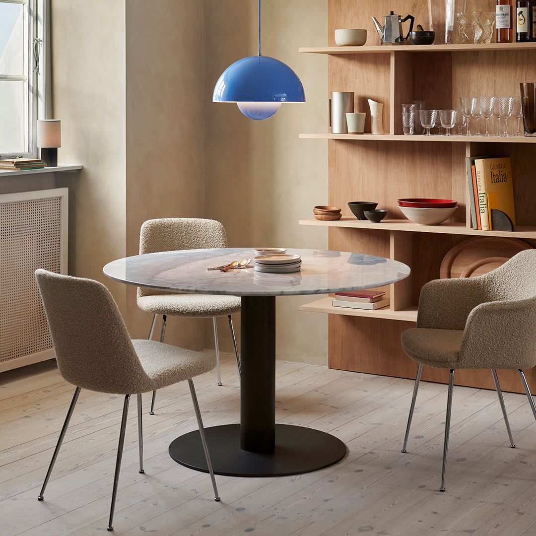 "Round marble table with a black base, surrounded by beige chairs and accented with a blue pendant light."